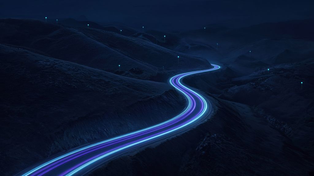 Carretera de noche entre colinas con estelas de luz de tráfico